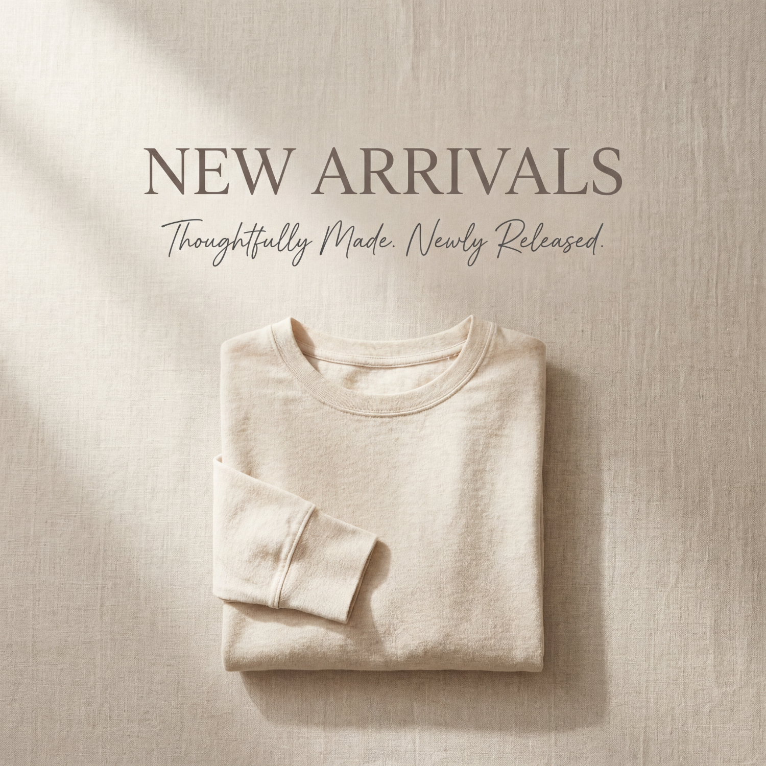 Folded cream-colored sweatshirt displayed on a textured neutral fabric background, representing newly released apparel.